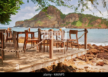 Estate cafe concetto di sfondo. Tavolo in legno e sedie a sdraio sulla spiaggia Foto Stock