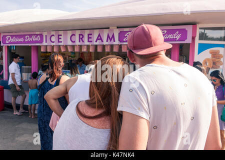 Vista posteriore di una giovane coppia in attesa in un gelato in stallo. Southend-on-Sea, Essex, Regno Unito Foto Stock