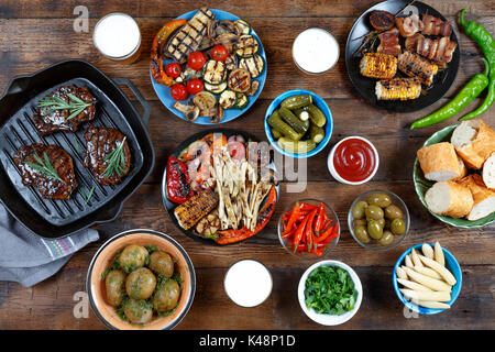 Tavolo per la Cena con grigliata di carne, bbq, verdure, insalate, salse, spuntini e birra, vista dall'alto Foto Stock