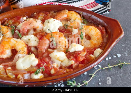 Forno supportato di gamberi con feta, pomodoro, paprica, timo in una tradizionale forma di ceramica su un sfondo astratto. Mangiare sano concetto. Stile di vita mediterranea. Foto Stock