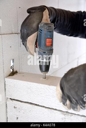 Il muratore utilizzando un cacciavite a batteria per la foratura di una vite in un calcestruzzo aerato parete di blocchi. Foto Stock