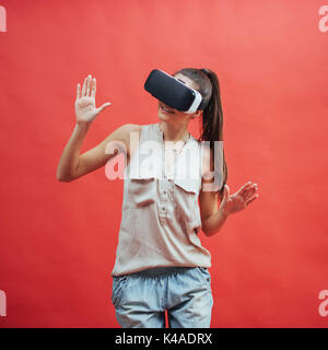 Una giovane donna con un dispositivo VR su uno sfondo di colore rosso in studio Foto Stock