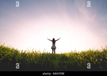 Donna libera alzando le mani al tramonto dorato. La libertà e il concetto di successo. Ragazza rilassarsi e godersi la natura Foto Stock