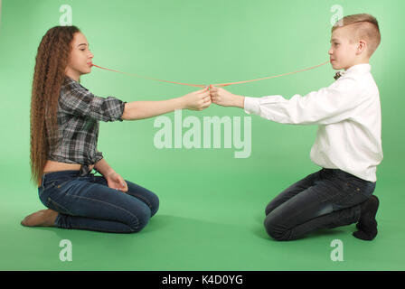 Ragazzo e ragazza stiramento da gomma da masticare che egli porta nella sua bocca isolati su sfondo verde Foto Stock