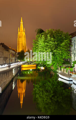 Vista della torre illuminata della chiesa di Nostra Signora a Bruges di notte con la riflessione in un canale. Foto Stock