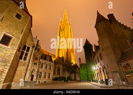 Vista della torre illuminata della chiesa di Nostra Signora a Bruges di notte con il Museo Gruuthuse edifici come primo piano. Foto Stock