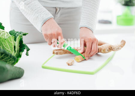 La donna la cottura di cibi sani nella sua cucina lei è affettare un fresco radice di zenzero con un coltello Foto Stock