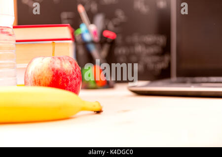 Si torna a scuola concetto. Ancora in vita con i libri di scuola e apple, banana e laptop contro di Blackboard Foto Stock