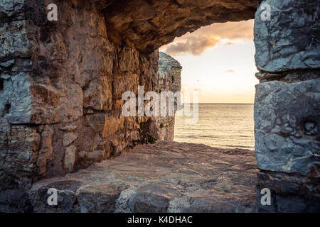 Le antiche rovine sfondo con scenic tramonto sul mare attraverso l antico castello finestra con cielo drammatico e vista prospettica con effetto di luce alla fine Foto Stock