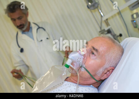 I medici che assiste i pazienti con mascherina di ossigeno nella camera di ospedale Foto Stock