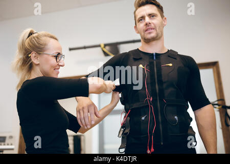 Ritratto di donna sorridente mettendo tuta ems sul giovane uomo Foto Stock