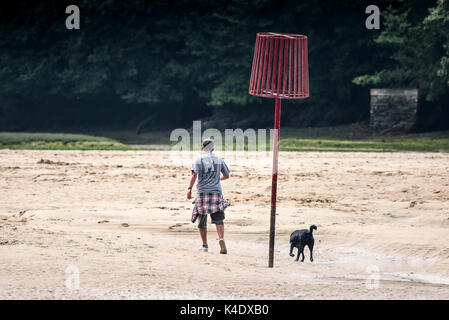 Gannel estuary - un uomo e il suo cane a camminare attraverso la parte esposta del letto del fiume del fiume gannel a bassa marea in Newquay, Cornwall. Foto Stock