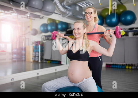 Ritratto di felice donna incinta il sollevamento barbell con il suo allenatore personale Foto Stock