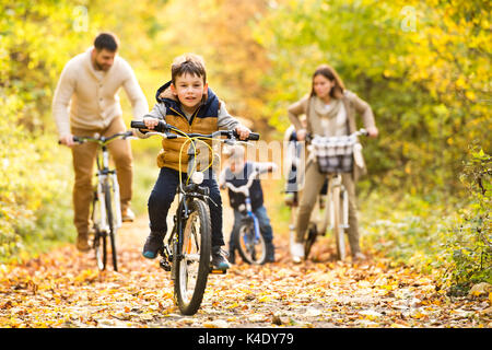 Famiglia giovane in vestiti caldi in bicicletta nel parco di autunno Foto Stock