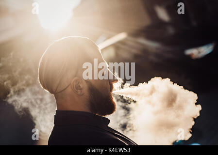 Uomo Barbuto in una tuta in città vaping Foto Stock