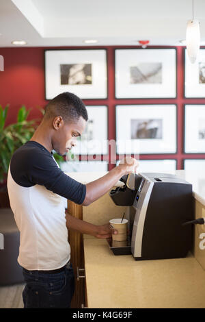 Closeup Ritratto, giovane ragazzo rendendo caldo o caffè ghiacciato con la macchina, isolata all'interno di fondo interna. Lunedì mattina la caffeina rush Foto Stock