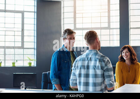 Tre casualmente vestito ufficio giovani collaboratori sorridente e parlare insieme mentre in piedi in un luminoso ufficio moderno Foto Stock