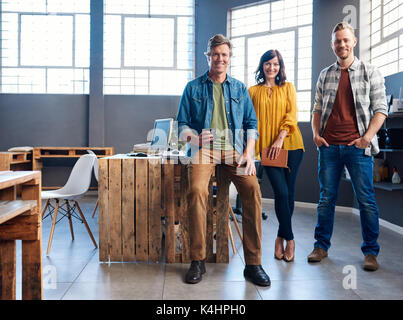 Ritratto di tre casualmente vestito giovani colleghi di ufficio sorridente con fiducia mentre si lavora insieme in un grande ufficio moderno Foto Stock