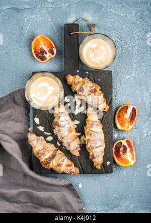 Tradizionale stile italiano home colazione. latte in bicchieri, croissant alle mandorle e rosso sanguinosa arance siciliane oltre il cemento tabella testurizzata Foto Stock