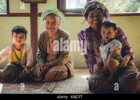 Il popolo della vita rurale nella campagna di Myanmar. Nonna, la madre ed i suoi due bambini seduti sul pavimento della loro casa prima di un pasto. Foto Stock