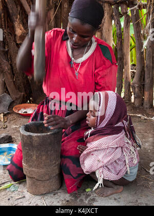 Una donna usa un tradizionale pestello di legno e di mortaio per macinare il caffè tostato in grani, Etiopia, Africa Foto Stock