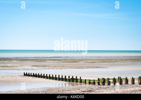 Un vuoto che la spiaggia di ciottoli a marea di declino con muschio groyne in legno che conducono al mare su una luminosa e soleggiata giornata di primavera. Foto Stock