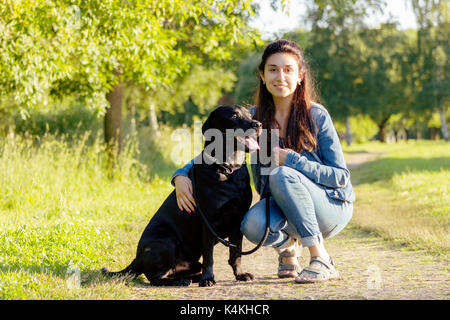 Bella giovane donna in posa con il suo nero labrador retriever sul sentiero in estate Foto Stock