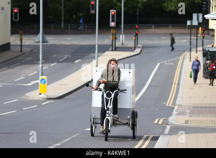 Bianco uomo middleaged con dreadlocks a cavallo di un triciclo per le strade di Brighton. Foto Stock