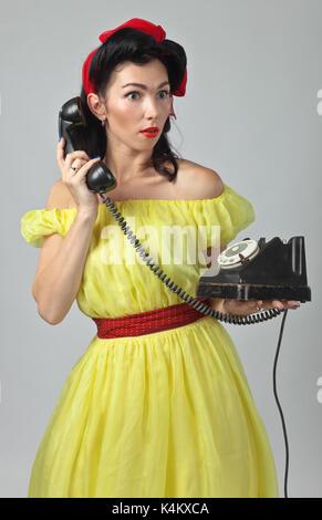 Bella bruna donna nel pin up con perfetto stile di capelli e portare la conversazione tramite telefono vintage.espressivo delle espressioni facciali. Foto Stock