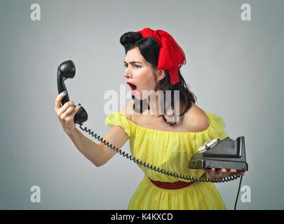 Giovane donna urlando in un telefono .Bella bruna nel pin up con perfetto stile di capelli e portare la conversazione tramite telefono vintage.viso espressivo expr Foto Stock