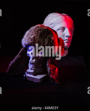 Un colorato ancora la vita di un cranio artificiale e un volto femminile statua. di blu e di rosso le luci in studio e composizione artistica Foto Stock