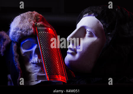 Un colorato ancora la vita di un cranio artificiale e un volto femminile statua. di blu e di rosso le luci in studio e composizione artistica Foto Stock