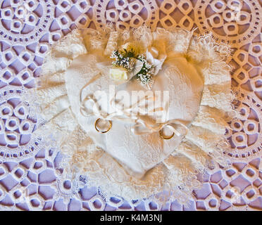 Doppio oro anelli vincolati su un cuscino bianco bianco a forma di cuore Foto Stock