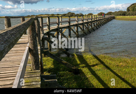 La gente camminare su una passerella di legno su velme ad alta marea a a Aberlady Bay natura locale riserva, East Lothian costa, Scotland, Regno Unito Foto Stock