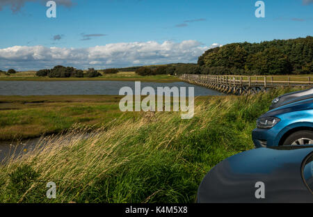 Auto parcheggiate a Aberlady Bay natura locale riserva, East Lothian, Scozia con una passerella di legno su velme ad alta marea Foto Stock