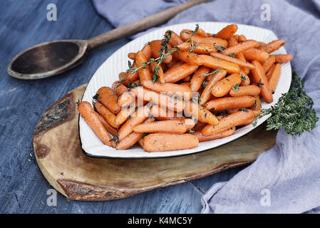 Glassato al miele baby carote con un vecchio rustico cucchiaio di legno e il timo. estrema profondità di campo con il fuoco selettivo su carote in primo piano. Foto Stock