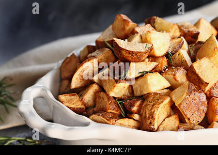 Patate arrosto tagliate in quarti e conditi con rosmarino e sale marino. estrema profondità di campo con il fuoco selettivo sul primo piano. Foto Stock