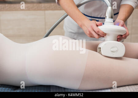 Donna in speciale tuta bianca getting anti cellulite massaggio in una spa salone. gpl e body contouring il trattamento in clinica. lipomassage procedura su fema Foto Stock