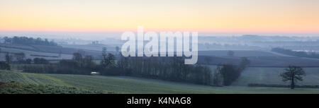 Il bagliore rosa del tramonto su un effetto smerigliato e nebbioso Northamptonshire paesaggio guardando verso Northampton è avvolta nella nebbia all'orizzonte, Inghilterra. Foto Stock