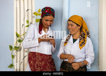 Due donne uzbeke con lo smartphone in abito tradizionale con testa sciarpe, Bukhara, Uzbekistan Foto Stock