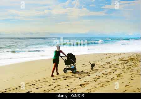 Donna con carrozzina e cane a piedi sulla spiaggia. Isola di Bali, Indonesia Foto Stock