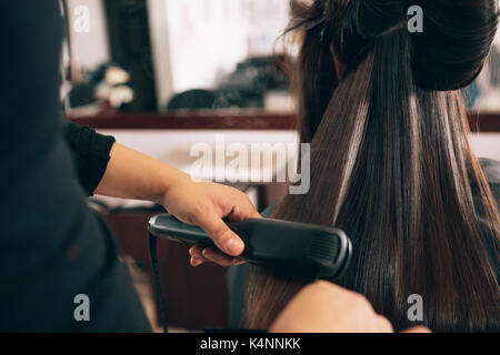 Parrucchiere usando un capello raddrizzati per lisciare i capelli. Hair stylist lavorando su una donna capelli stile al salone. Foto Stock