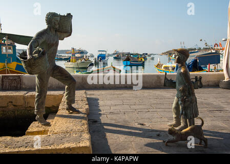 Marsaxlokk, Malta - agosto 23, 2017: statua in bronzo di un pescatore e un ragazzo con un gatto presso il porto della baia di marsaxlokk nell isola di Malta Foto Stock