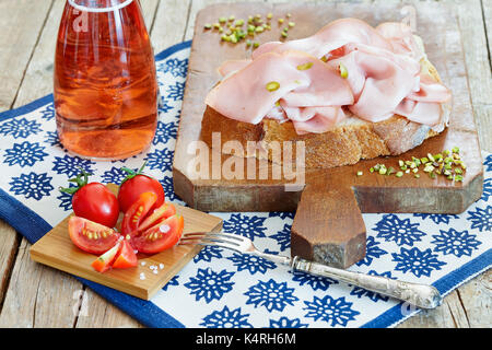Fresh cut mortadella con pistacchi sulla fetta di pane, insieme con pomodorini e rose vino spumante. Foto Stock