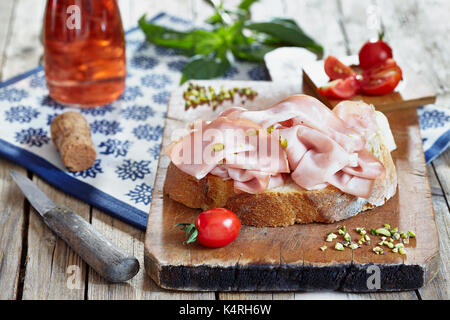 La mortadella con pistacchi freschi sulla fetta di pane con pomodori ciliegia, basilico e rose vino spumante. Foto Stock