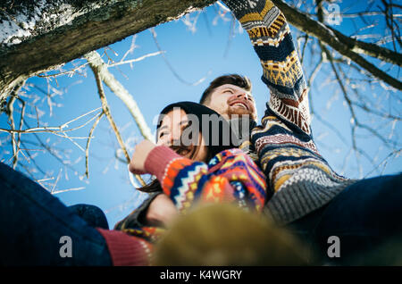 Gioiosa carino coppia abbraccia. giovane in un maglione abbraccia una ragazza da seduto sul ramo di albero in inverno. Il concetto di un rapporto di successo e di ha Foto Stock