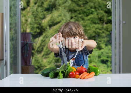 Carino piccolo ragazzo seduto al tavolo entusiasti di farine vegetali, bene o male abitudini alimentari, nutrizione e alimentazione sana nozione Foto Stock