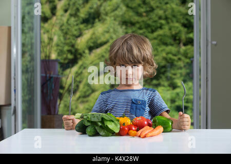 Carino piccolo ragazzo seduto al tavolo, accigliata su farine vegetali, cattive abitudini alimentari, nutrizione e alimentazione sana nozione Foto Stock