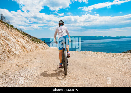 Vista posteriore della donna bike ghiaia luminosa strada costiera in Croazia. Foto Stock