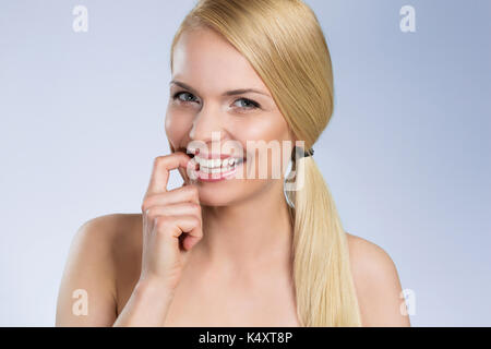Parte anteriore Ritratto di giovane donna bionda di mordere il dito sorridente Foto Stock